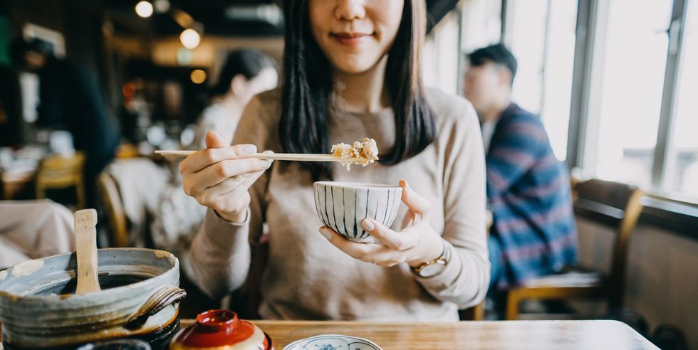 close up shot of smiling young woman enjoying japanese cuisine with various side dishes, miso soup and green tea in restaurant