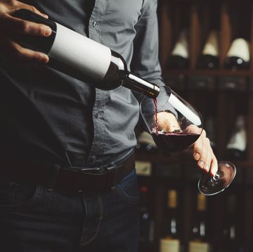 close up shot of sommelier pouring red wine from bottle in glass on underground cellar background
