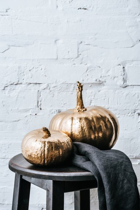 close up shot of two halloween pumpkins painted in golden metallic in front of white brick wall