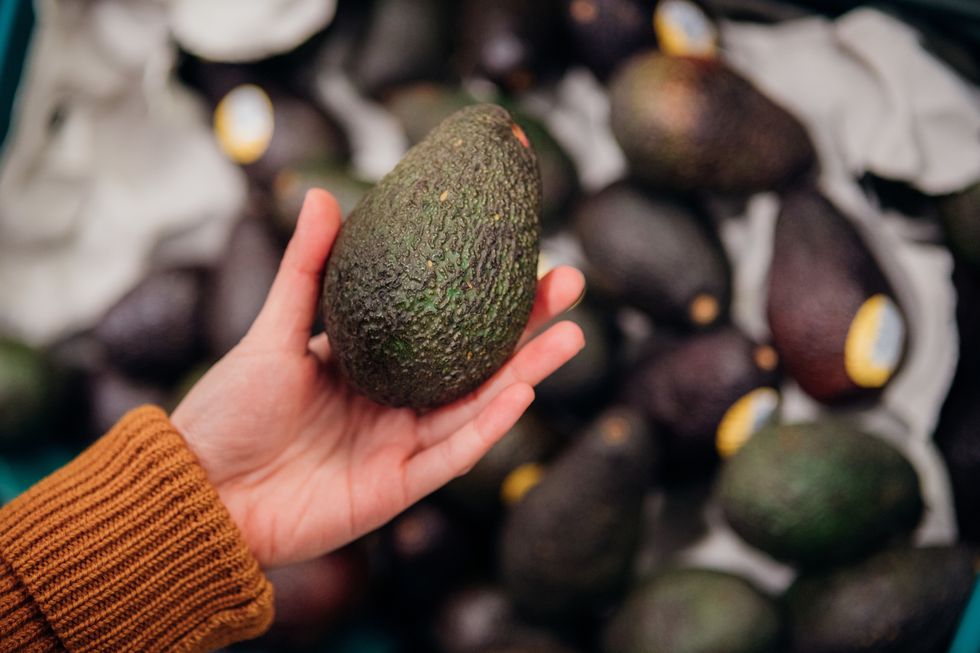 close up shot of woman’s hand holding avocado in grocery store