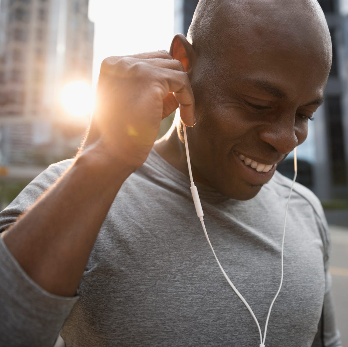 Close up smiling male runner listening to music with earbud headphones on urban street