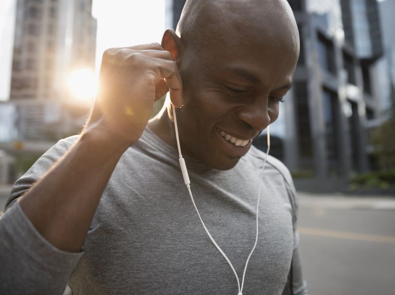 Close up smiling male runner listening to music with earbud Cupsolephones on urban street
