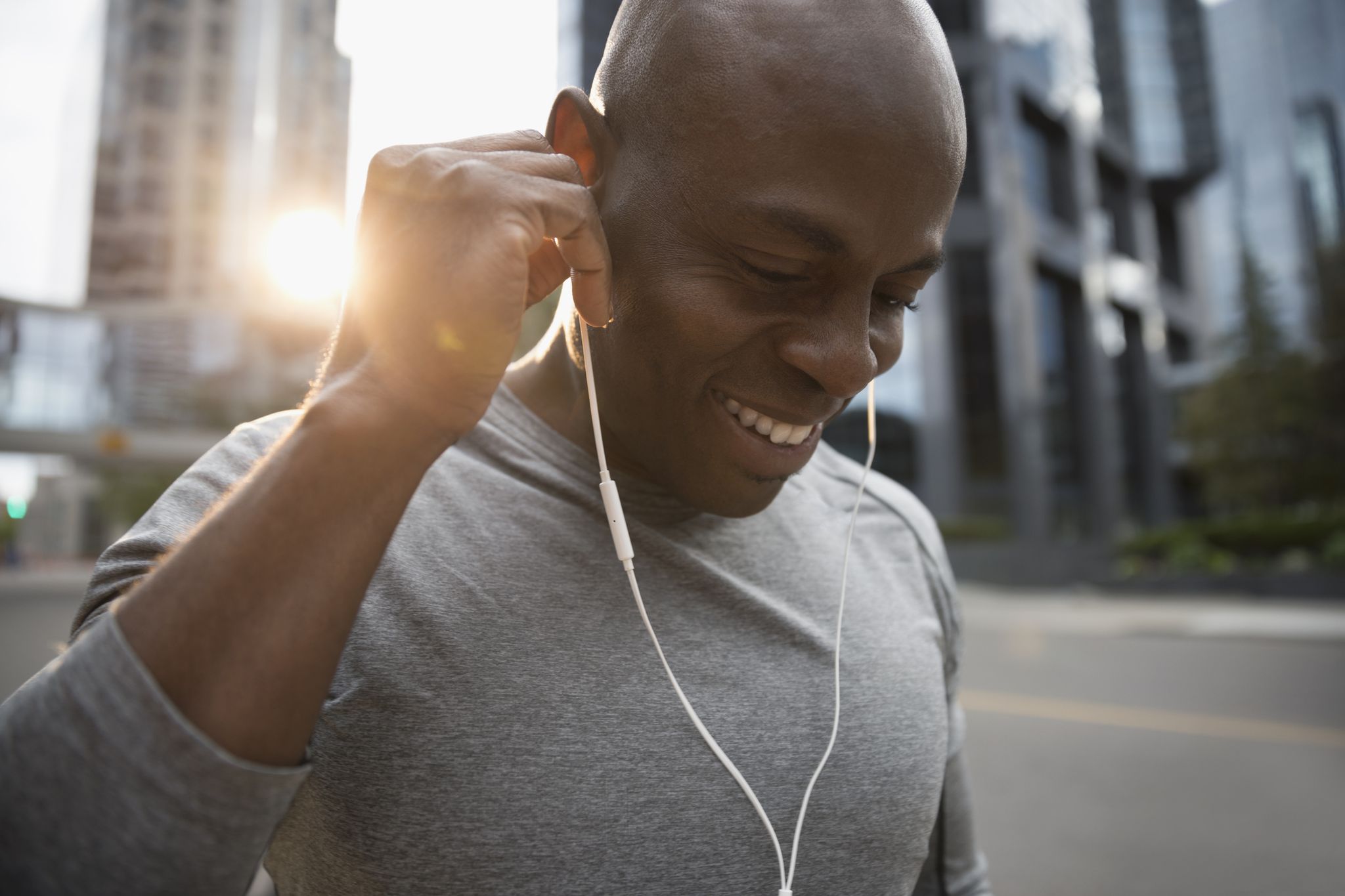 Close up smiling male runner listening to music with earbud headphones on urban street