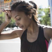 Close up tired female runner wiping sweat from forehead on urban street