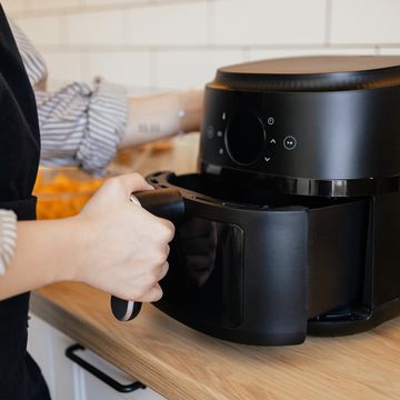 close up view of a woman putting a basket into an air fryer for cooking