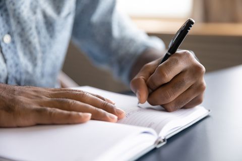 close up view of african left handed businessman writing in notebook