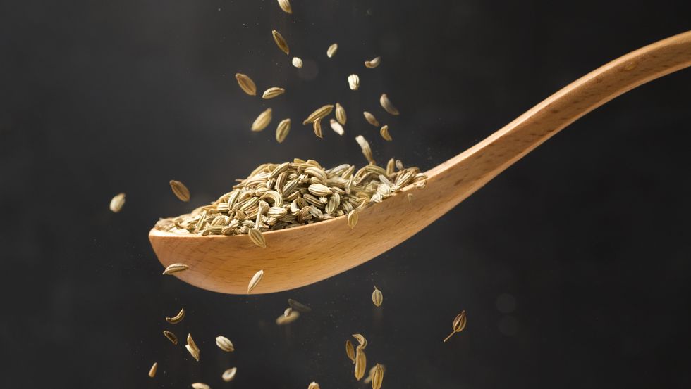 Close up view of cumin in wooden spoon.