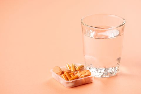 close-up view of glass of water and pills in container on pink