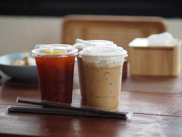 close up view of ice cubes in cold brewed coffee cappuccino in plastic cup put on bamboo wooden desk blurred background, drink beverage