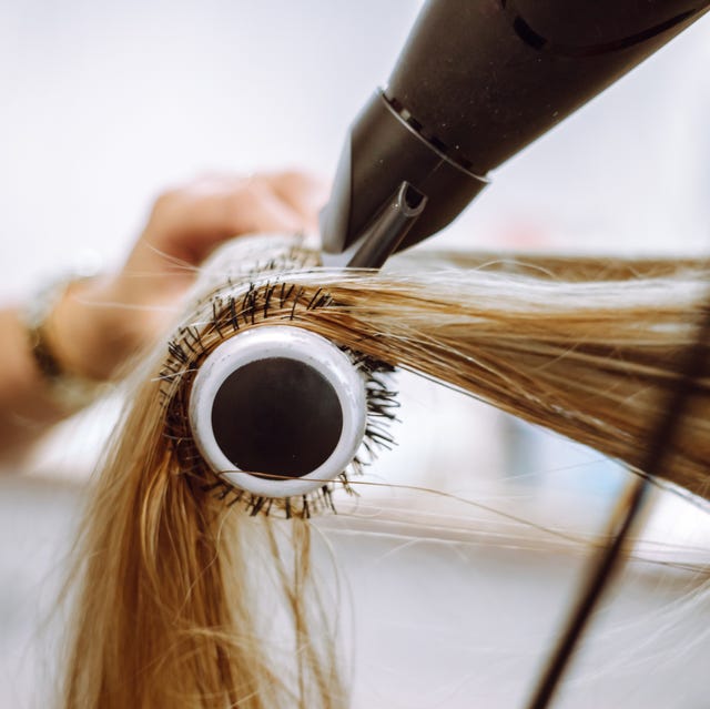 close up view of lock of long blond hair on hairbrush being dried by blow dryer