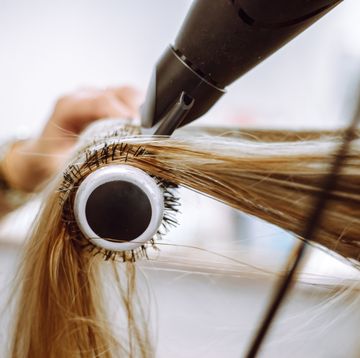 close up view of lock of long blond hair on hairbrush being dried by blow dryer