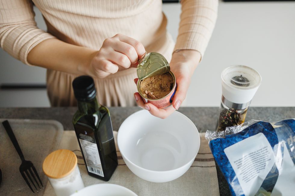 close up view of unrecognisable woman opening a can of tuna in a kitchen.