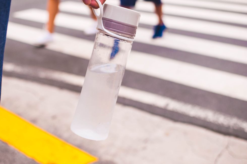a close up view of woman's hand holding a reusable water bottle on the street