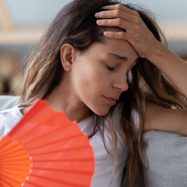 close up woman sitting on couch reducing heat using fan