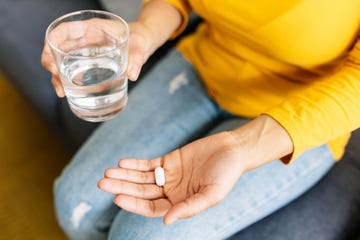 close up van vrouw met glas water in een hand, witte pil in andere hand