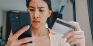 concerned woman looking at phone and holding gift card
