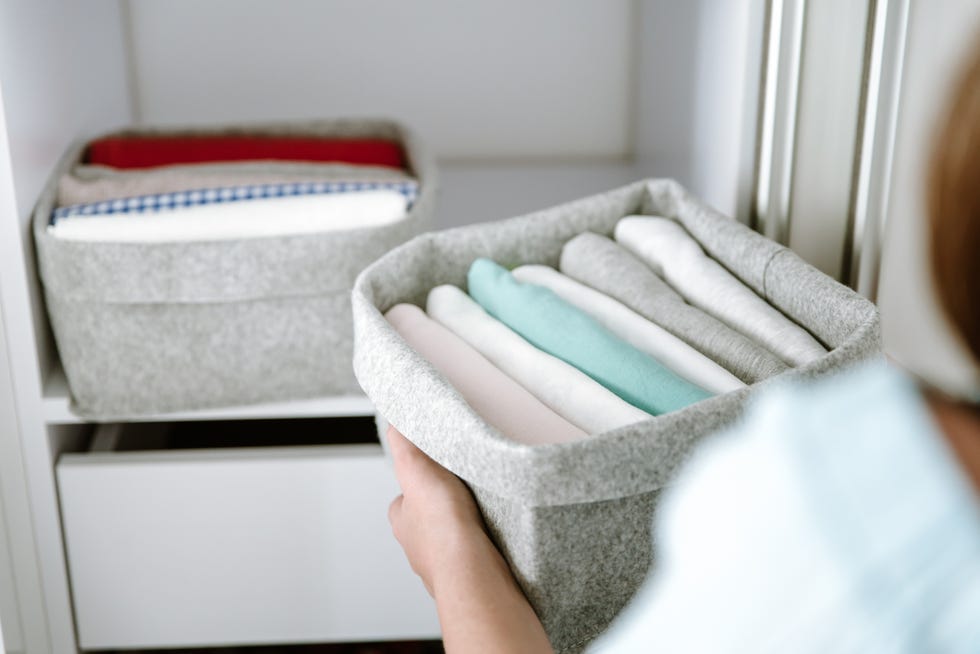 woman organizing clothes in wardrobe, putting shirts in boxes. concept of order, minimalist closet, japanese t shirt folding system and clothes storage
