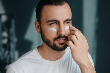 closeup of bearded handsome man applying under eye cream at home good looking man using beauty products moisturising or nourishing skin