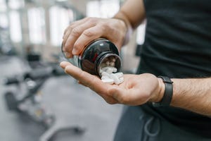 Closeup of sporty muscular man arms showing sports and fitness supplements, capsules, pills, gym background. Healthy lifestyle, medicine, nutritional supplements and people concept