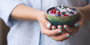Closeup of woman's hands holding cup with organic yogurt with blueberries, coconut and fresh mint. Homemade vanilla yogurt in girl's hands. Breakfast, snack. Healthy eating and lifestyle concept
