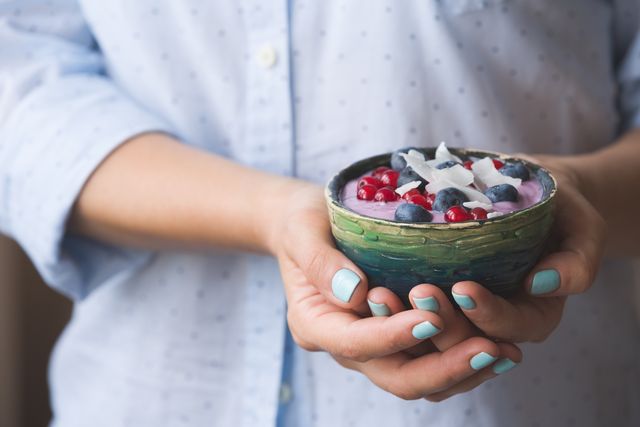 Closeup of woman's hands holding cup with organic yogurt with blueberries, coconut and fresh mint. Homemade vanilla yogurt in girl's hands. Breakfast, snack. Healthy eating and lifestyle concept