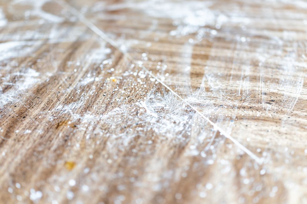 Closeup of wooden table surface in kitchen with messy dirty cooking preparation bakery dusted with starch, flour background