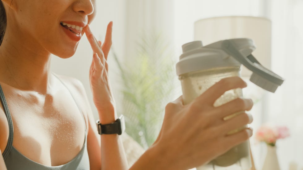 closeup of young asian athletic woman drinking protein shake on sofa in living room at home diet and healthy food