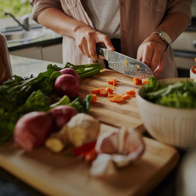 closeup of young female hands chopping fresh vegetables on chopping board while in modern kitchen preparing a healthy meal to boost immune system and fight off coronavirus