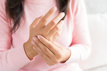 closeup woman sitting on sofa holds her wrist hand injury, feeling pain health care and medical concept