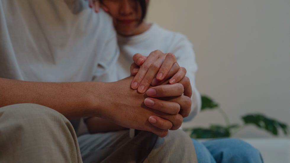 closeup young asian woman supporting depressed frustrated boyfriend together on sofa in living room at home night lifestyle spend time house