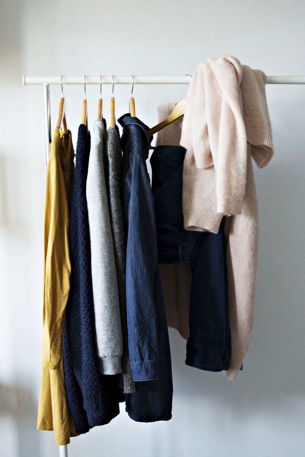 clothes hanging on rack with a pale pink sweater tossed over the rack