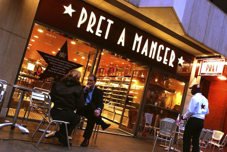 a central london pret a manager store with two people sitting outside and a worker heading back in to the shop