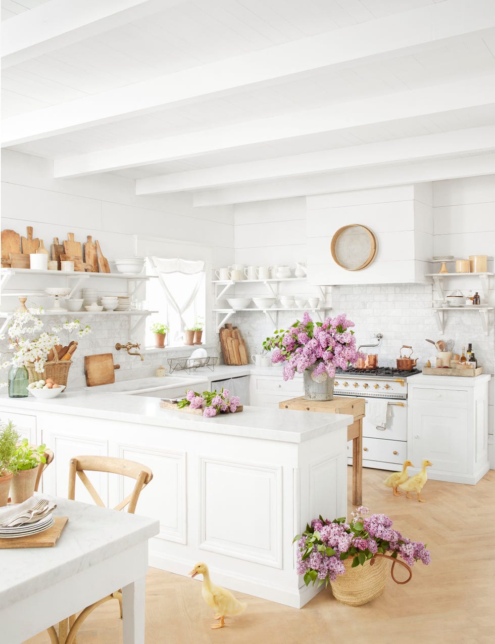 a white farmhouse kitchen with purple flowers and live ducks on the floor