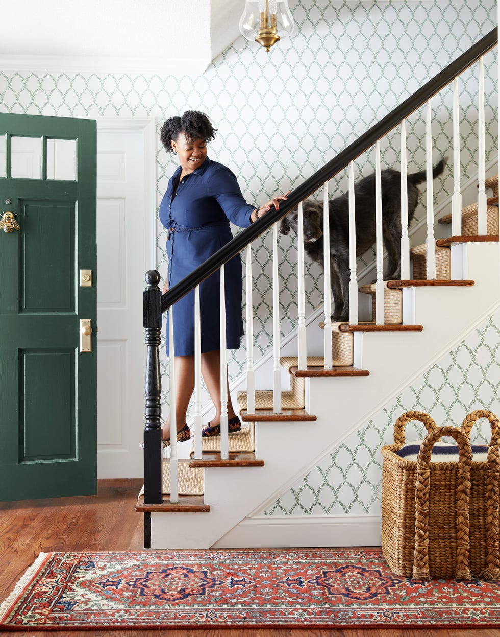 wallpapered stairwell with green and white wallpaper and green door, woman and dog on stairs