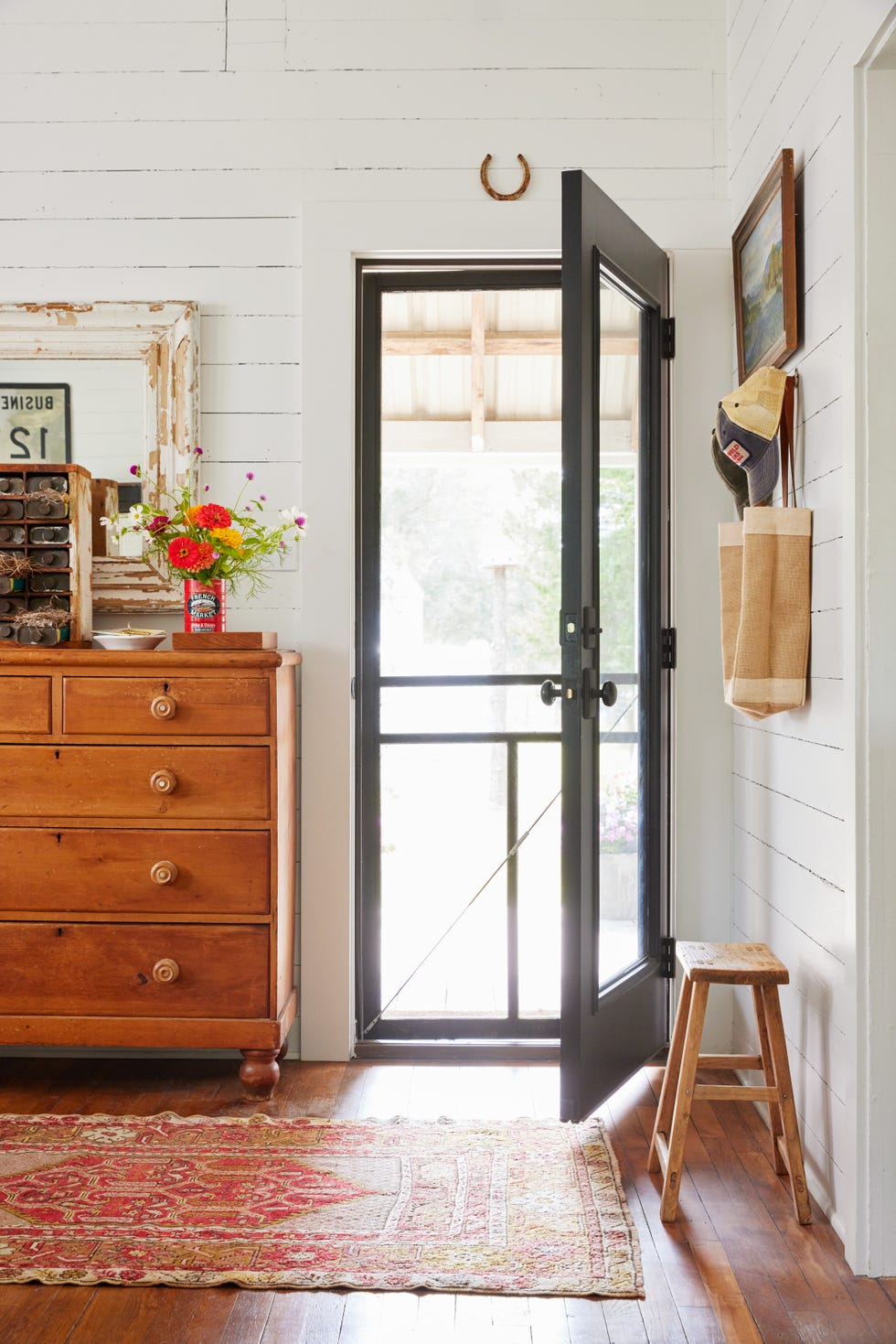 white entryway with screen door, pine dresser for storage stacked with antique decor