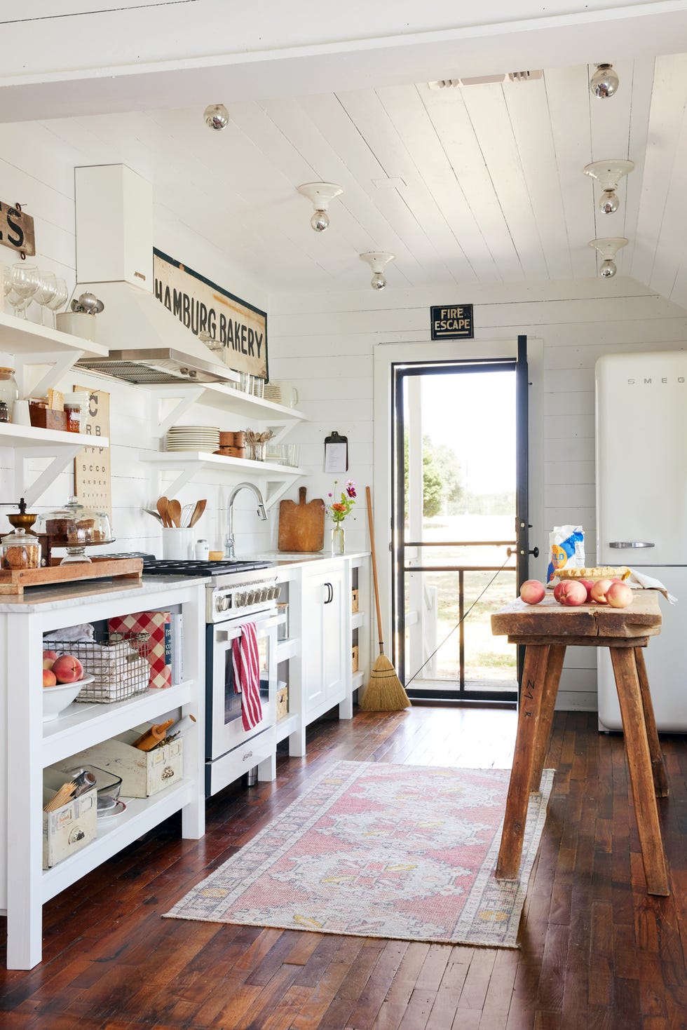 white kitchen with open shelving, roadside and farmstand signs, and a long antique island made from a work table