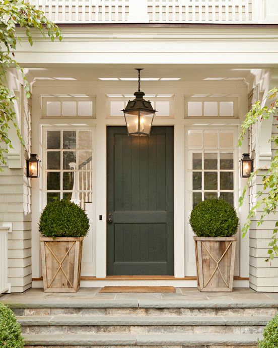 close up of green, wooden front door of county home with a pair of potted boxwoods flanking it