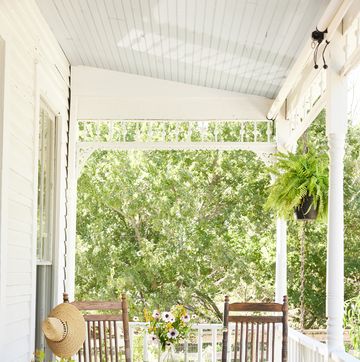 classic white covered farmhouse porch with rocking chairs, dogs, container plants