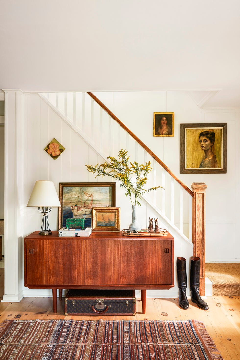 farmhouse entry with white stairs, statement mid century wood console piled with antiques