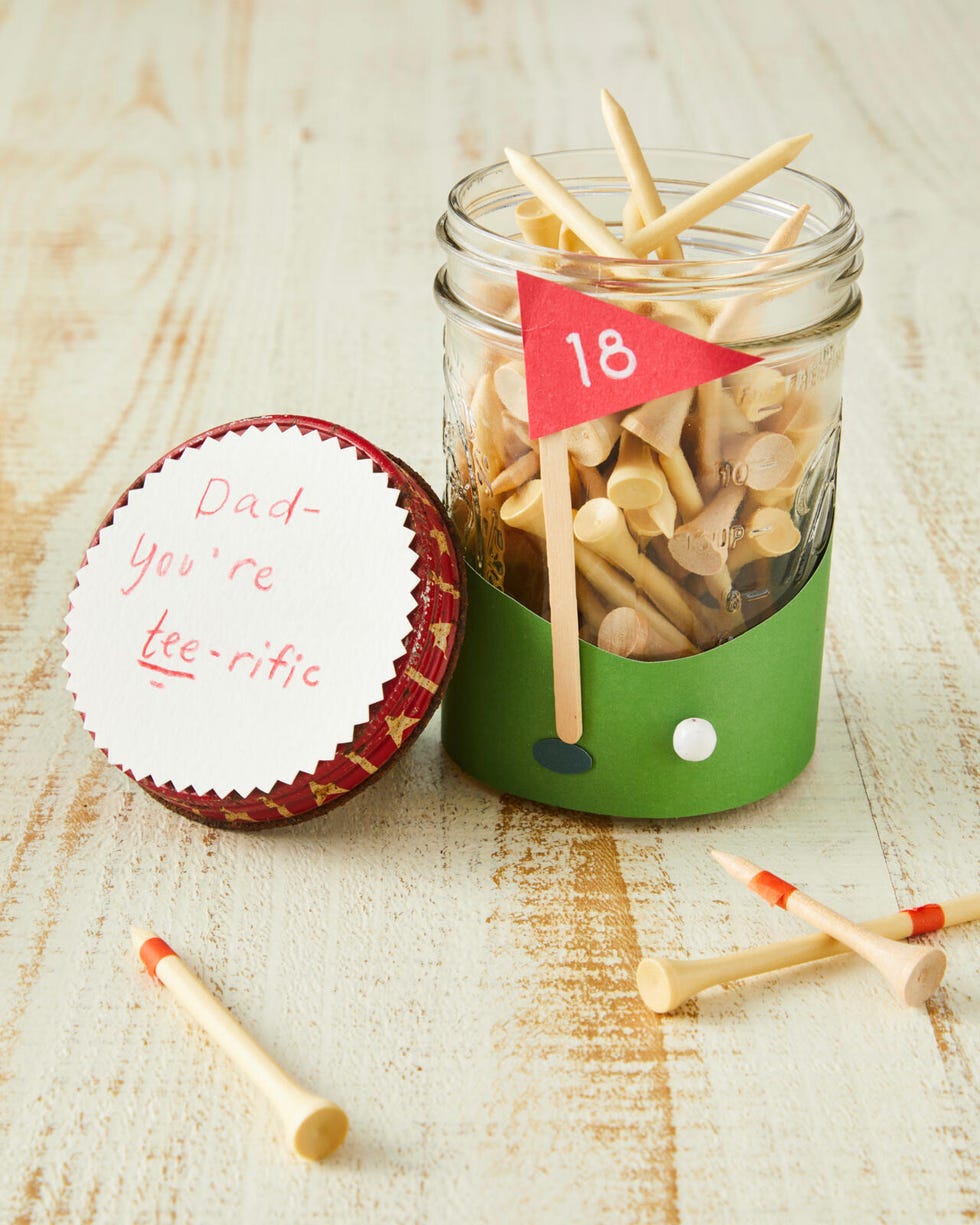 A mason jar decorated with paper to look like a putting green filled with golf tees