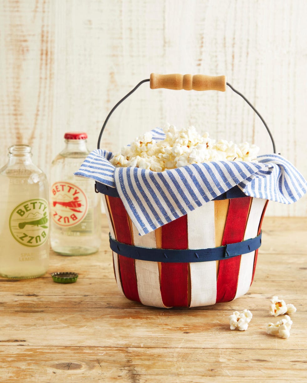 A small vintage apple basket painted red, white and blue, lined with napkins and filled with popcorn.