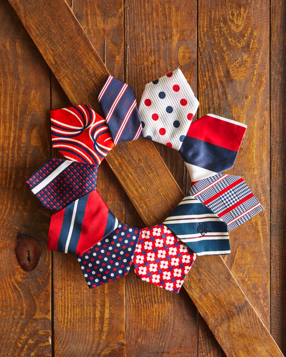 A wreath made from vintage red, white and blue neckties hangs on a brown wooden door