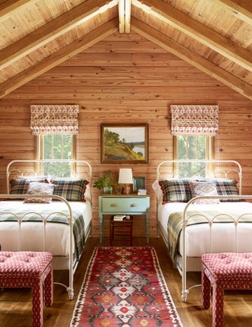 this bedroom designed by bruce fox features knotty pine walls, antique white iron beds, and custom ikat benches sitting at the foot of each bed