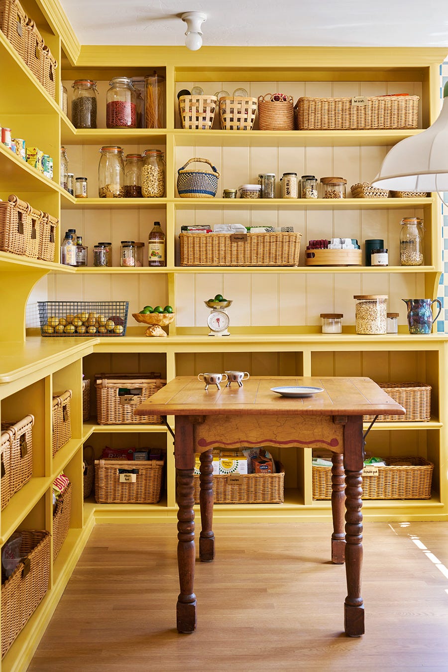 yellow kitchen pantry with large wooden island and shelves stocked with baskets and food