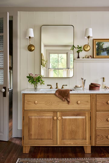 bathroom with light wood vanity, marble sink, simple mirror, two sconces with shades flanking mirror, creamy white walls