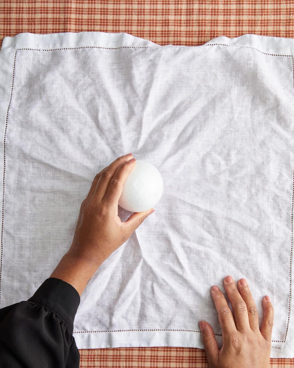 hands holding a small foam ball over a white napkin