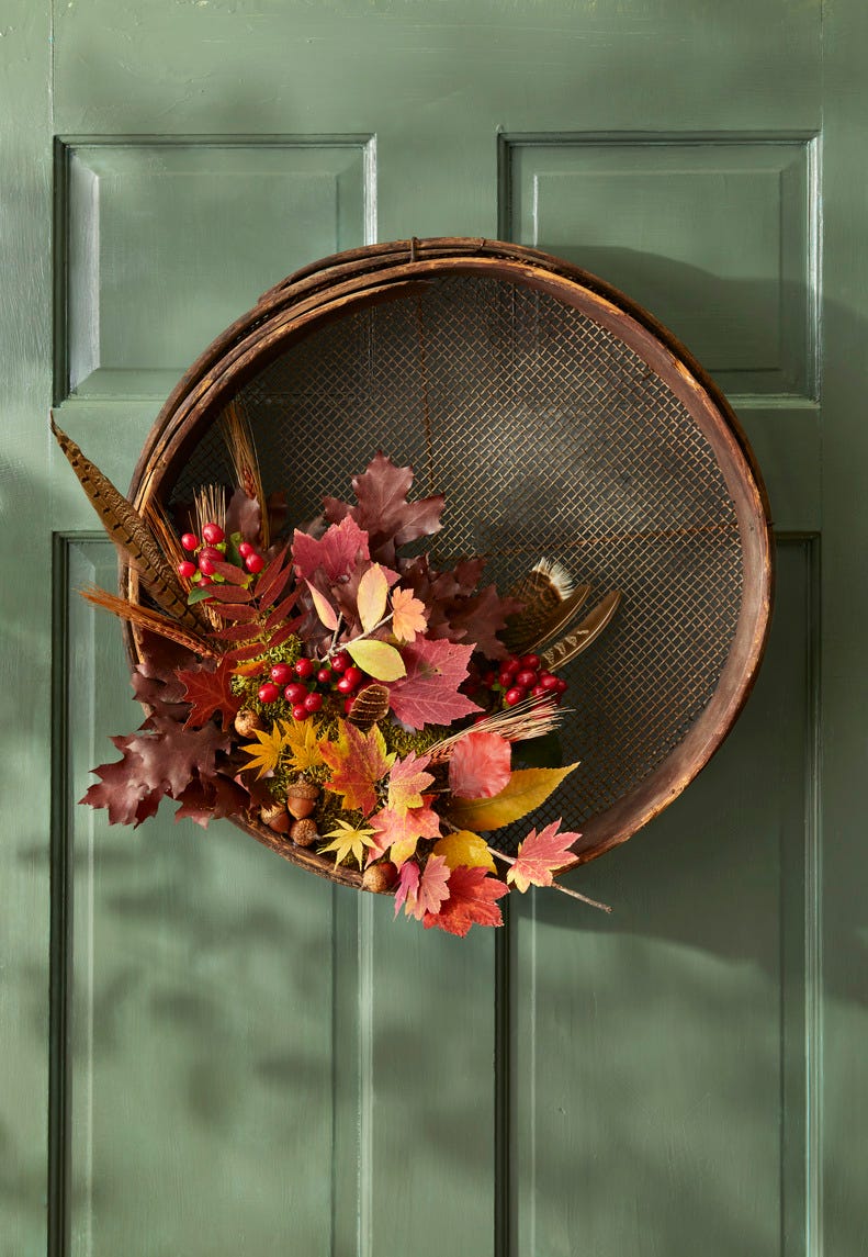 grain sifter wreath on dark sage green door with fall foliage tucked into the side