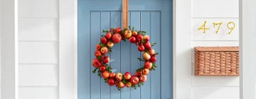 a wreath made from apples and boxwood on a light blue door