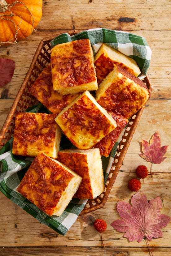 squares of cheddar cornbread in a wicker basket that is line with a green and white gingham napkin