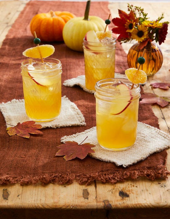 cider mule cocktails in small mason jars with ice and and apple slice with a skewer of candied ginger in the glass